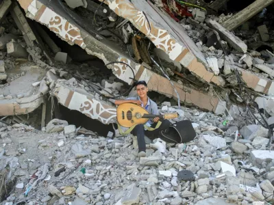 Palestinian teenager Youssef Saad sits on the rubble of his house as he plays oud to bring joy to children, amid Israel-Hamas conflict, in Jabalia refugee camp in the northern Gaza Strip September 2, 2024. REUTERS/Mahmoud Issa