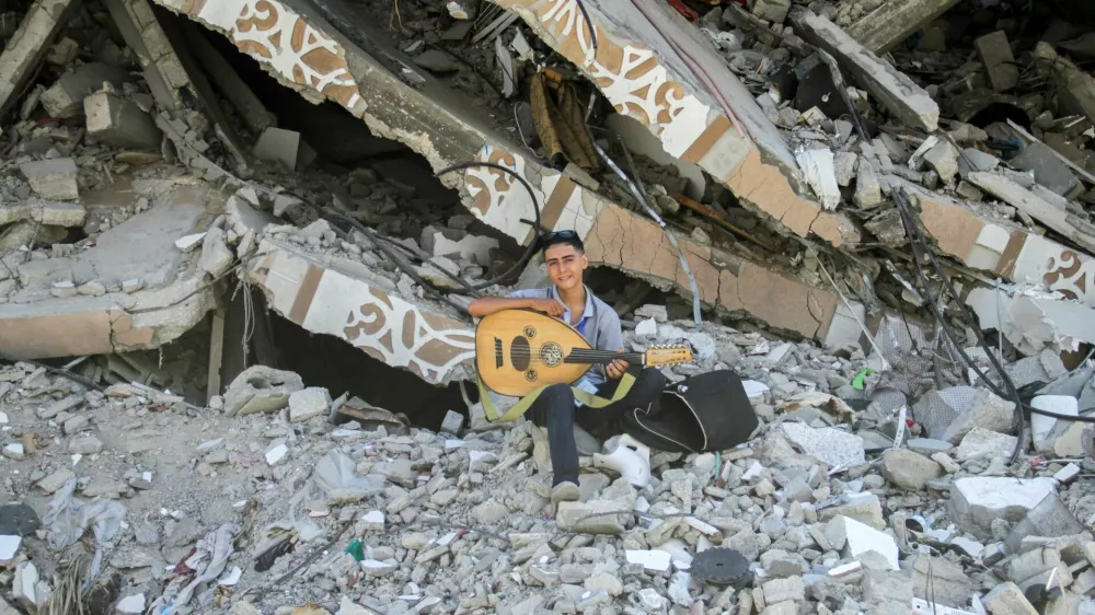 Palestinian teenager Youssef Saad sits on the rubble of his house as he plays oud to bring joy to children, amid Israel-Hamas conflict, in Jabalia refugee camp in the northern Gaza Strip September 2, 2024. REUTERS/Mahmoud Issa