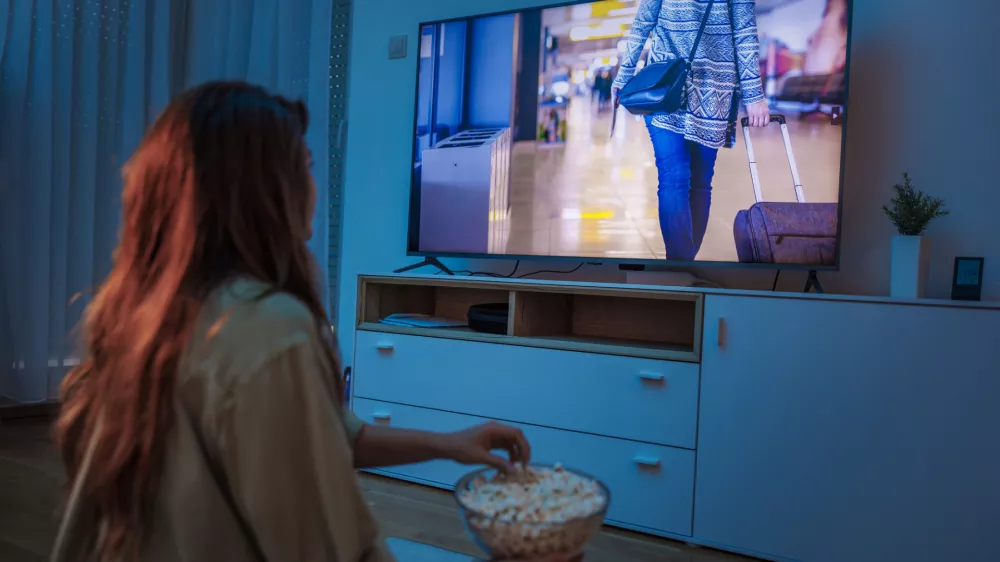 Young woman enjoying leisure time at home at night, watching a movie on TV and eating popcorn / Foto: Getty Images, Vladans