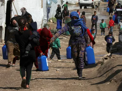 FILE PHOTO: Syrian refugees walk as they carry containers at an informal tented settlement in the Bekaa valley, Lebanon March 12, 2021. Picture taken March 12, 2021. REUTERS/Mohamed Azakir/File Photo