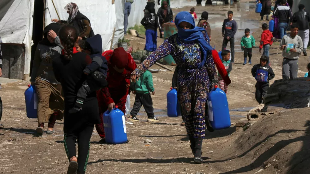 FILE PHOTO: Syrian refugees walk as they carry containers at an informal tented settlement in the Bekaa valley, Lebanon March 12, 2021. Picture taken March 12, 2021. REUTERS/Mohamed Azakir/File Photo