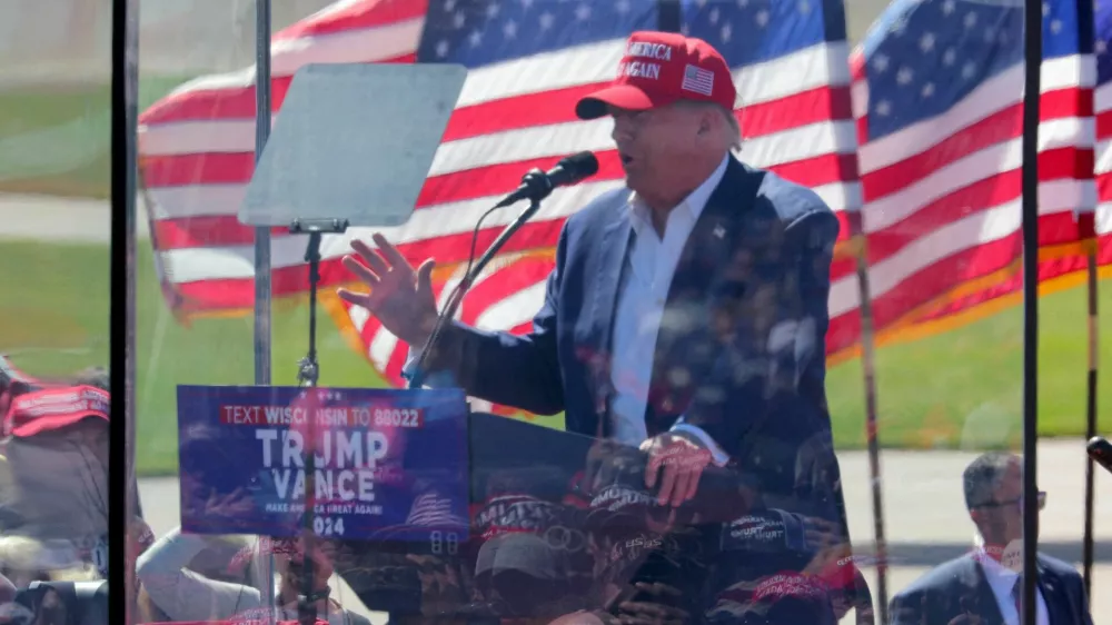 People are reflected in protective glass as they listen to Republican presidential nominee and former U.S. President Donald Trump as he speaks during a rally in Mosinee, Wisconsin, U.S. September 7, 2024. REUTERS/Brian Snyder