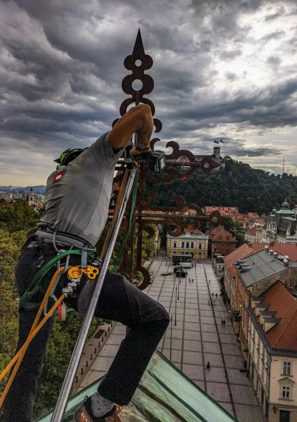 Izkušeni plezalec opravlja tudi druga dela na višini. V začetku poletja je zamenjal uršulinski križ, ki bedi nad Kongresnim trgom. Foto: DrevoRez