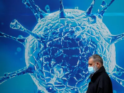 FILE PHOTO: A man wearing a protective face mask walks past an illustration of a virus outside a regional science centre, as the city and surrounding areas face local restrictions in an effort to avoid a local lockdown being forced upon the region, amid the coronavirus disease (COVID-19) outbreak, in Oldham, Britain August 3, 2020. REUTERS/Phil Noble/File Photo