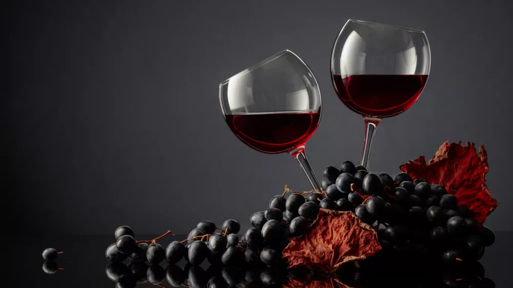 Glasses of red wine and blue grapes on a black background. Copy space. / Foto: Igorr1