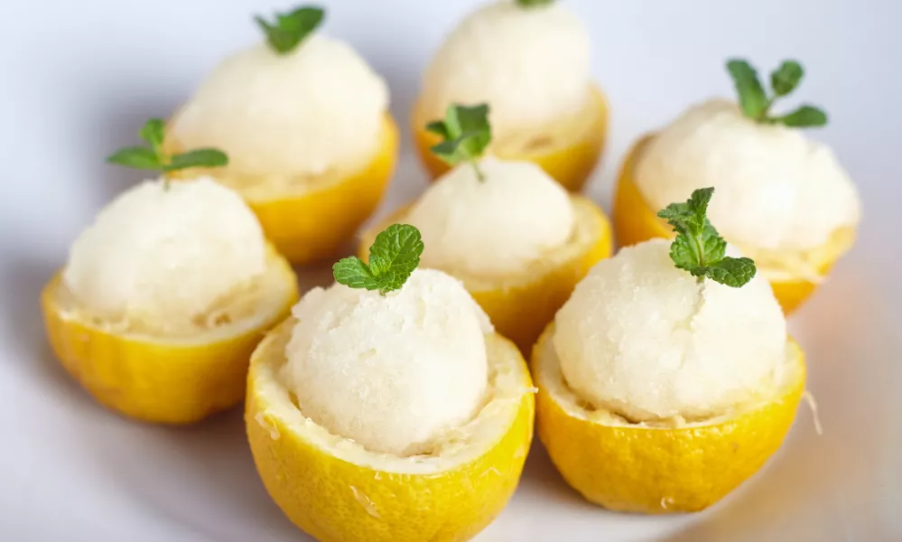 Lemon sorbet or ice cream inside fresh lemons decorated with mint leaves on big white plate / Foto: Alexbai