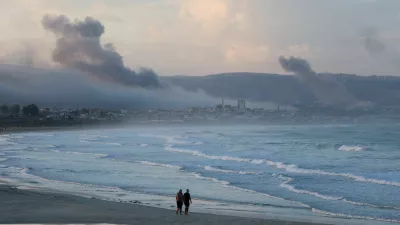 People walk at a beach as smoke billows over southern Lebanon following Israeli strikes, amid ongoing cross-border hostilities between Hezbollah and Israeli forces, as seen from Tyre, southern Lebanon September 23, 2024. REUTERS/Aziz Taher