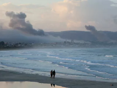 People walk at a beach as smoke billows over southern Lebanon following Israeli strikes, amid ongoing cross-border hostilities between Hezbollah and Israeli forces, as seen from Tyre, southern Lebanon September 23, 2024. REUTERS/Aziz Taher   TPX IMAGES OF THE DAY