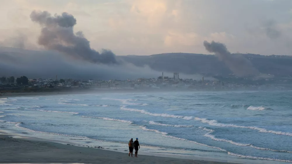 People walk at a beach as smoke billows over southern Lebanon following Israeli strikes, amid ongoing cross-border hostilities between Hezbollah and Israeli forces, as seen from Tyre, southern Lebanon September 23, 2024. REUTERS/Aziz Taher   TPX IMAGES OF THE DAY