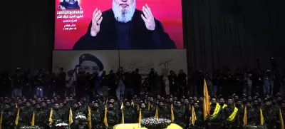 FILE - Hezbollah fighters stand behind the coffin of their top commander Fouad Shukur, who was killed by an Israeli airstrike on July 30, as Hezbollah leader Sayyed Hassan Nasrallah speaks through a screen during Shukur's funeral in a southern suburb of Beirut, Lebanon, Aug. 1, 2024. (AP Photo/Hussein Malla, File)