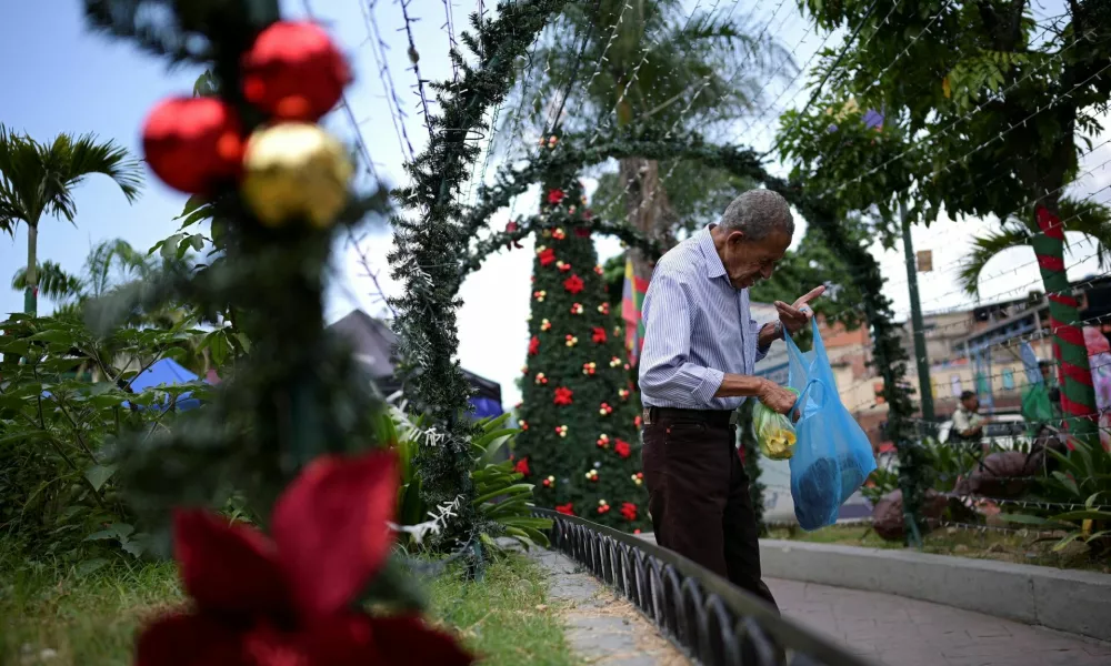 A man checks a plastic bag with food in front of Christmas decorations at a public square, as the Christmas season kicks off as per a decree of Venezuela's President Nicolas Maduro, in Caracas, Venezuela October 1, 2024. REUTERS/Gaby Oraa   TPX IMAGES OF THE DAY