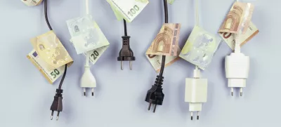 Electric power plugs with Euro banknotes on them hanging on light blue background. Energy efficiency, power consumption, electricity cost, and expensive energy concept. / Foto: Vejaa