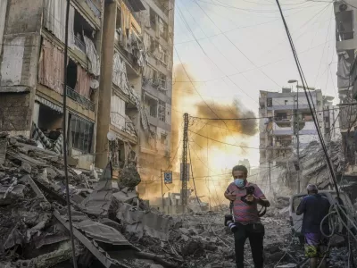 A photographer runs for cover as a smoke raises in the background following an Israeli airstrike in Dahiyeh, Beirut, Lebanon, Friday, Oct. 4, 2024. (AP Photo/Hassan Ammar)