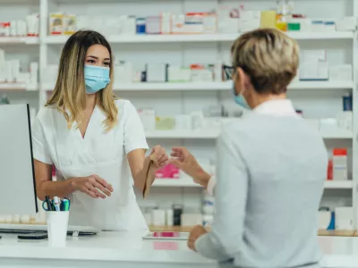 Female pharmacist wearing protective mask and serving a customer patient in a pharmacy and packing drugs in a paper bag