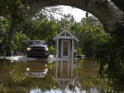 A pick up drives past a guard gate on a flooded street in Siesta Key, Fla., following the passage Hurricane Milton, Thursday, Oct. 10, 2024. (AP Photo/Rebecca Blackwell)