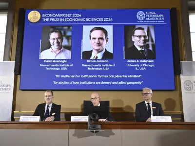 Academy of Sciences permanent secretary Hans Ellegren, center, Jakob Svensson, left, and Jan Teorell, of the Nobel assembly announce the Nobel memorial prize in economics winners, Daron Acemoglu, Simon Johnson and James A Robinson, seen on screen, during a press meeting at the Royal Swedish Academy of Sciences in Stockholm, Sweden, Monday Oct. 14, 2024. (Christine Olsson/TT News Agency via AP)