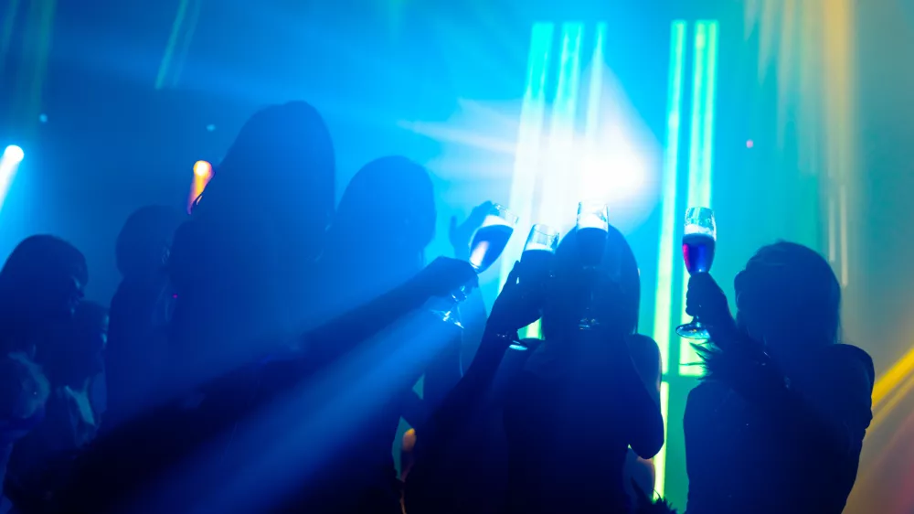 Silhouette image of people dance in disco night club to music from DJ on stage. New year night party and nightlife concept.