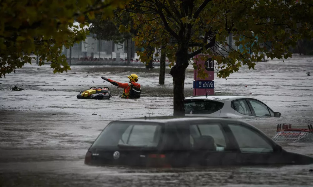 17 October 2024, France, Givors: Firefighters wade through the floodwaters, past partially flooded cars parked in a flooded shopping center. Photo: Jean-Philippe Ksiazek/AFP/dpa