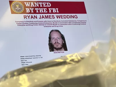 An image of former Canadian Olympic snowboarder Ryan Wedding, 43, who is a fugitive and been charged with allegedly running and participating in a transnational drug trafficking operation, is displayed on a video monitor along with bricks of cocaine, foreground, during a news conference at the FBI offices in Los Angeles, Thursday, Oct. 17, 2024. (AP Photo/Damian Dovarganes)