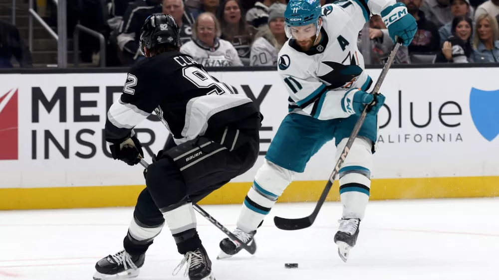 Oct 24, 2024; Los Angeles, California, USA; San Jose Sharks center Luke Kunin (11) moves the puck against Los Angeles Kings defenseman Brandt Clarke (92) during the third period at Crypto.com Arena. Mandatory Credit: Jason Parkhurst-Imagn Images