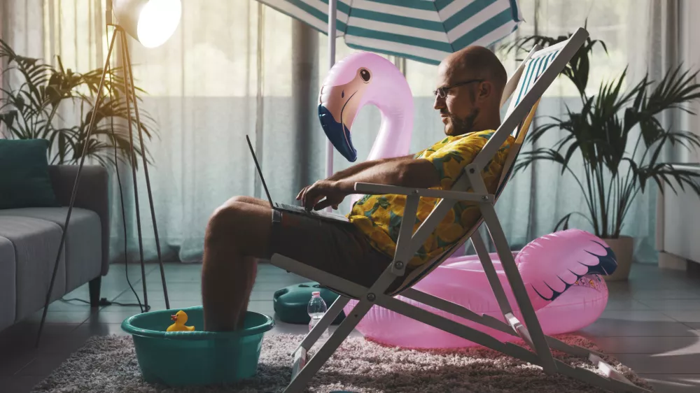 Delo od doma, Man spending summer vacations at home alone, he is sitting on the deckchair in the living room and working with a laptop