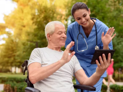 A nurse and an elderly patient who is sitting in a wheelchair, watching something interesting in the old man's tablet / Foto: Vadimguzhva