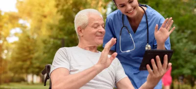 A nurse and an elderly patient who is sitting in a wheelchair, watching something interesting in the old man's tablet / Foto: Vadimguzhva