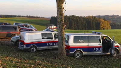 Police vehicles and a police helicopter stand near a field in the village Fraunschalg near Altenfelden, Austria, Monday, Oct. 28, 2024, after people were fatally shot in the area. (AP Photo/laumat/Matthias Lauber)