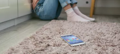 Mobile phone lying on the floor with unrecognizable sad little girl sitting behind. Selective focus on mobile in foreground / Foto: Doble-d