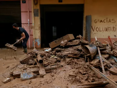 A man uses a broom next to mud-covered items and graffiti reading "Thank you volunteers", following heavy rains that caused floods, in Paiporta, near Valencia, Spain, November 3, 2024. REUTERS/Eva Manez