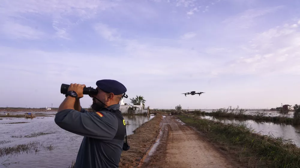 As the search for bodies continues, a Civil Guard looks though binoculars as a drone flies nearby at the mouth of the Poyo ravine in the La Albufera natural lake near Puerto de Catarroja, Valencia on the outskirts of Valencia, Spain, Tuesday, Nov. 5, 2024. (AP Photo/Alberto Saiz)