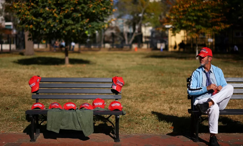 A man sits next to a bench with MAGA hats, after Republican Donald Trump won the U.S. presidential election, outside the White House in Washington, D.C., U.S., November 6, 2024. REUTERS/Hannah McKay   TPX IMAGES OF THE DAY