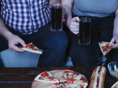 Emotional eating, alcohol addiction, depression, relationship problems. Overweight couple watching tv eating pizza and beer late in the night. Nerve food / Foto: Vadym Petrochenko