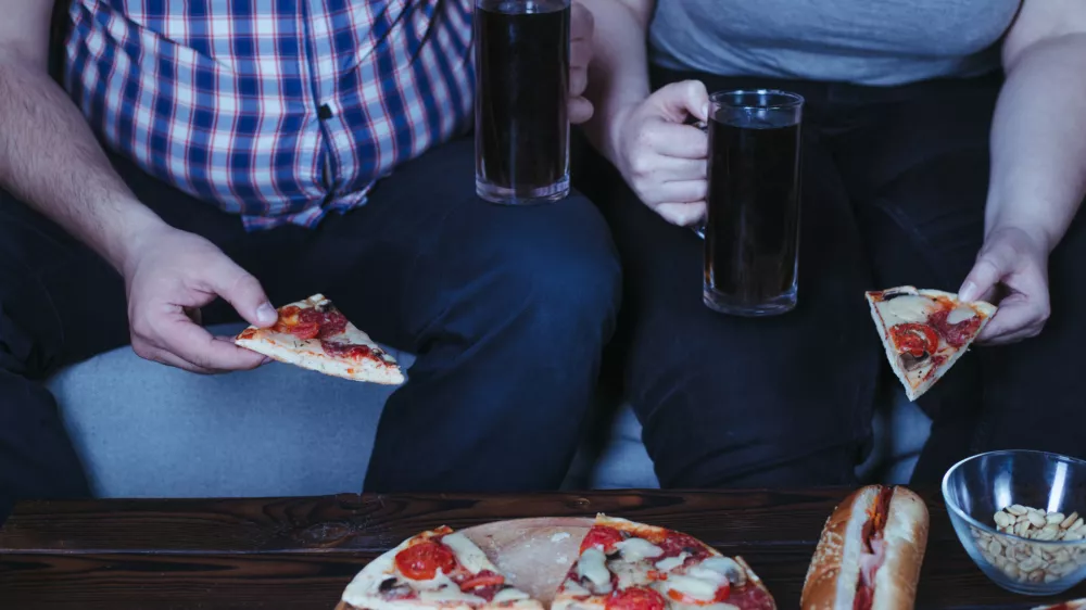 Emotional eating, alcohol addiction, depression, relationship problems. Overweight couple watching tv eating pizza and beer late in the night. Nerve food / Foto: Vadym Petrochenko