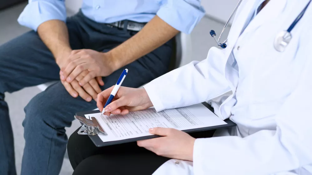 Female doctor holding application form while consulting man patient in hospital. Medicine and healthcare concept. / Foto: Andrei_r