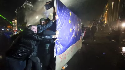 People hold a part of a fence with an EU flag as police use a water cannon to prevent protesters pouring into the streets following Georgian Prime Minister Irakli Kobakhidze's announcement, rallying outside the parliament building in Tbilisi, Georgia, Friday, Nov. 29, 2024. (AP Photo/Zurab Tsertsvadze)