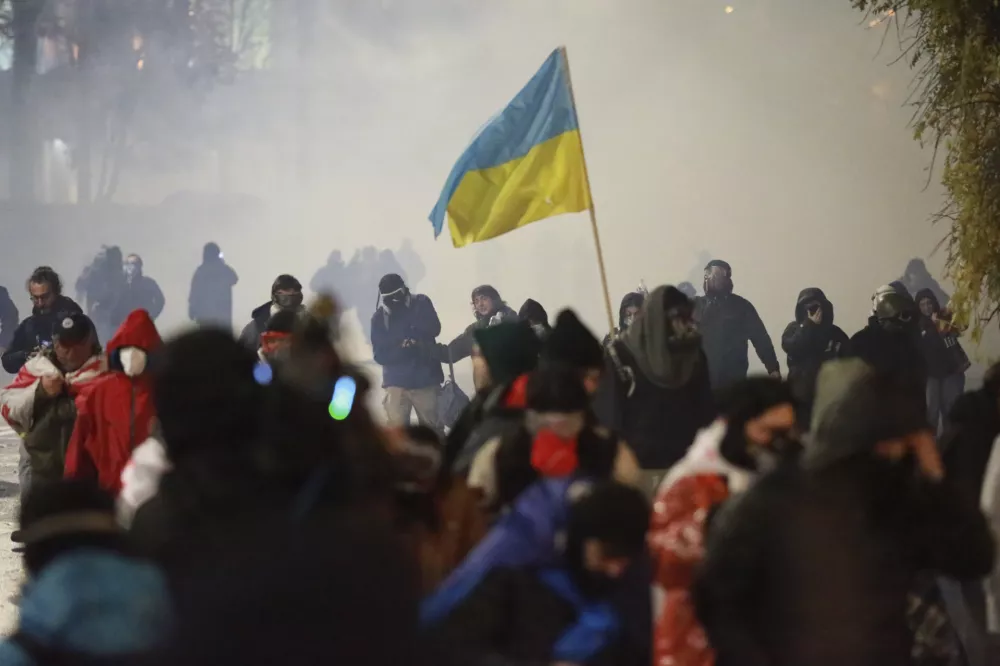 Demonstrators, one of them holding the Ukrainian national flag, run away from a cloud of tear gas during a rally against the government's decision to suspend negotiations on joining the European Union for four years in Tbilisi, Georgia, early Monday, Dec. 2, 2024. (AP Photo/Zurab Tsertsvadze)