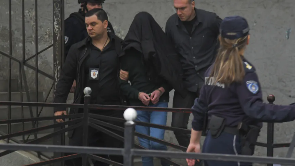 A suspect is escorted by police outside the Vladislav Ribnikar school in Belgrade, Serbia, Wednesday, May 3, 2023. Serbian police say a teenage boy opened fire at a school in central Belgrade, killing several people and injuring several more. (AP Photo)