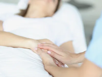 On bed lies a sick doctor sitting next to him and sympathetically holds hand. Euthanasia in world practice concept