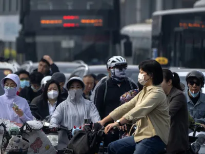 Commuters wearing face masks wait at an intersection in the central business district during the morning rush hour in Beijing, Friday, May 26, 2023. (AP Photo/Mark Schiefelbein)