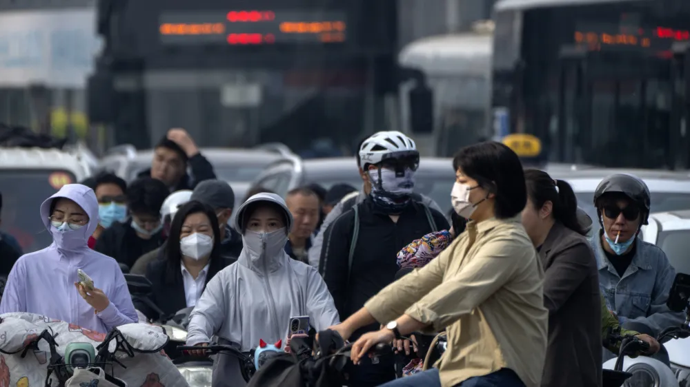 Commuters wearing face masks wait at an intersection in the central business district during the morning rush hour in Beijing, Friday, May 26, 2023. (AP Photo/Mark Schiefelbein)