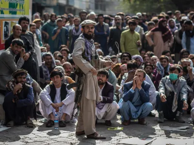 FILED - 22 September 2021, Afghanistan, Kabul: A Taliban security guard plays with a whip while standing in front of Afghan men waiting outside a bank to withdraw money. More than 1,000 civilians have been killed in Afghanistan since the Taliban returned to power in August of 2021, a United Nations report released on Tuesday shows. Photo: Oliver Weiken/dpa