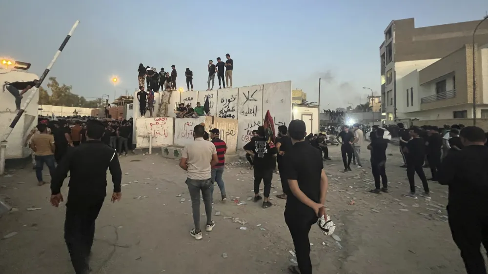 Protesters scale a wall at the Swedish Embassy in Baghdad Thursday, July 20, 2023. Protesters angered by the burning of a copy of the Quran stormed the embassy early Thursday, breaking into the compound and lighting a small fire. (AP Photo/Ali Jabar)