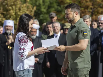 In this photo provided by the Ukrainian Presidential Press Office, Ukrainian President Volodymyr Zelenskyy, right, hands over the first passport for a girl during an event for marking Statehood Day in Mykhailivska Square in Kyiv, Friday, July 28, 2023. (Ukrainian Presidential Press Office via AP)