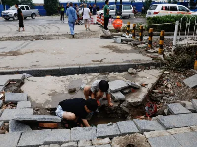 Children play near a hole on a road that is damaged after remnants of Typhoon Doksuri brought rains and floods in Beijing, China August 2, 2023. REUTERS/Tingshu Wang