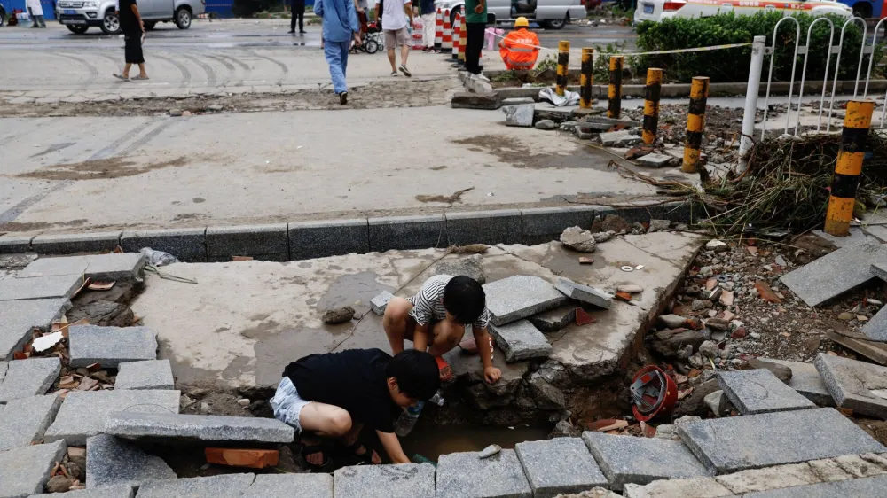 Children play near a hole on a road that is damaged after remnants of Typhoon Doksuri brought rains and floods in Beijing, China August 2, 2023. REUTERS/Tingshu Wang