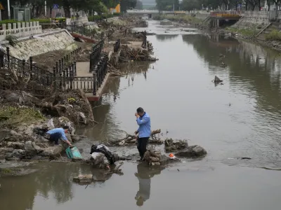 Residents wash their suitcase and belongings on a damaged bank of a canal clogged with flood debris in the aftermath of flood waters from an overflowing river in the Mentougou district on the outskirts of Beijing on Monday, Aug. 7, 2023. The death toll in recent flooding in China's capital rose, officials said Wednesday, as much of the country's north remains threatened by unusually heavy rainfall. (AP Photo/Andy Wong)