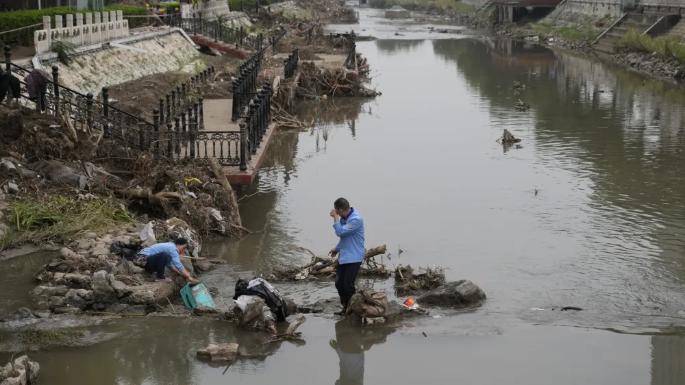 Residents wash their suitcase and belongings on a damaged bank of a canal clogged with flood debris in the aftermath of flood waters from an overflowing river in the Mentougou district on the outskirts of Beijing on Monday, Aug. 7, 2023. The death toll in recent flooding in China's capital rose, officials said Wednesday, as much of the country's north remains threatened by unusually heavy rainfall. (AP Photo/Andy Wong)