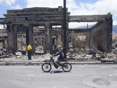 A boy rides along Main Street past wildfire damage on Friday, Aug. 11, 2023, in Lahaina, Hawaii. (AP Photo/Rick Bowmer)