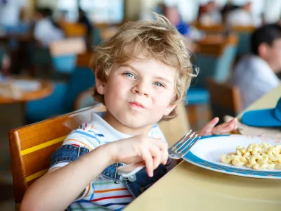 Cute healthy preschool kid boy eats pasta noodles sitting in school or nursery cafe. Happy child eating healthy organic and vegan food in restaurant. Childhood, health concept